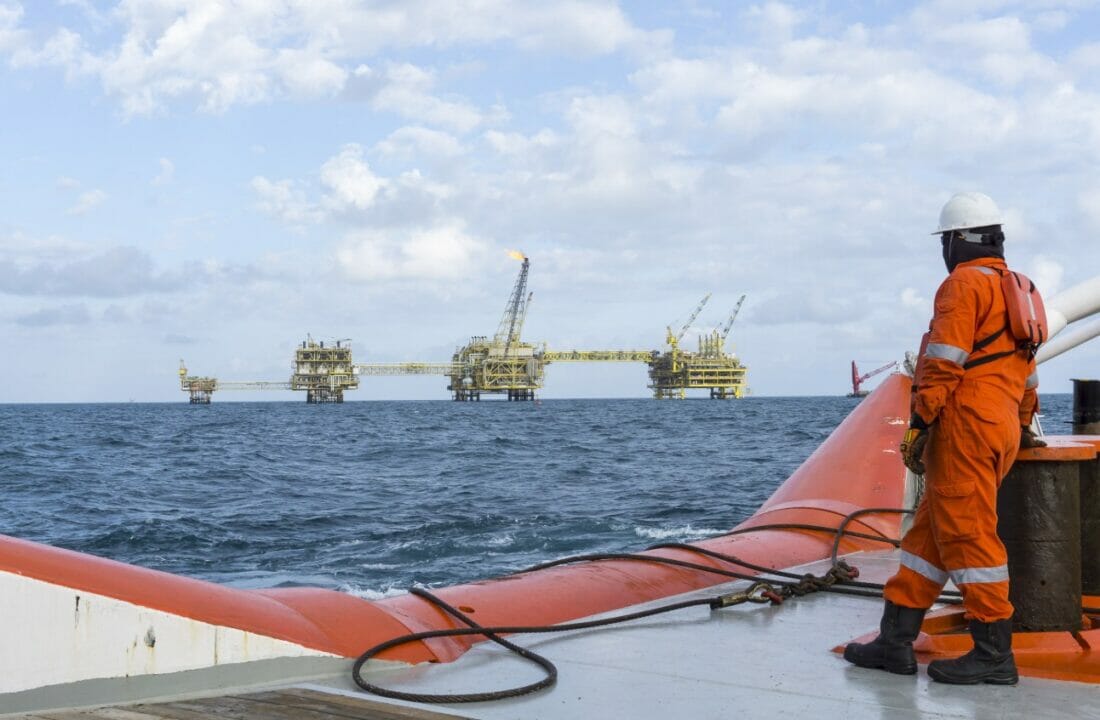 Homem em uma embarcação olhando para a plataforma de petróleo offshore em alto mar