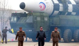 Líder norte-coreano caminha com oficiais militares em frente a um grande míssil balístico montado em um veículo de lançamento.