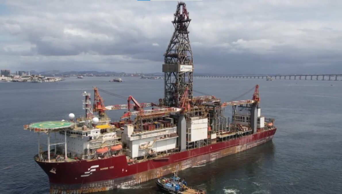 Navio-sonda Norbe VIII ancorado na Baía de Guanabara, com a ponte Rio-Niterói ao fundo e o Pão de Açúcar visível, em contraste com a paisagem urbana do Rio de Janeiro.