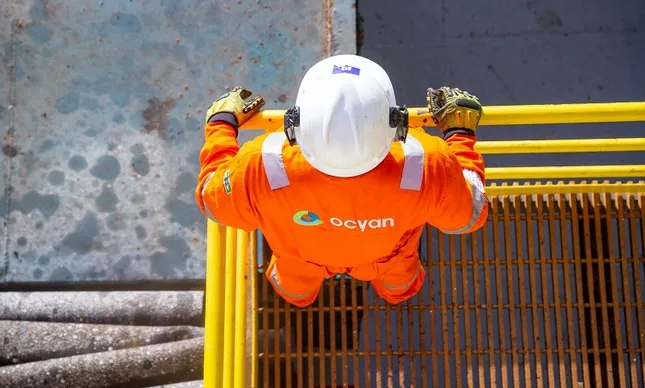 Trabalhador da Ocyan em uniforme laranja realizando manutenção em estrutura offshore em Macaé.