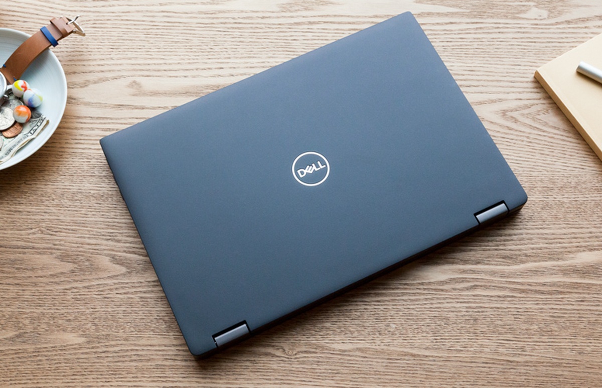 Notebook Dell fechado sobre mesa de madeira ao lado de itens de escritório
