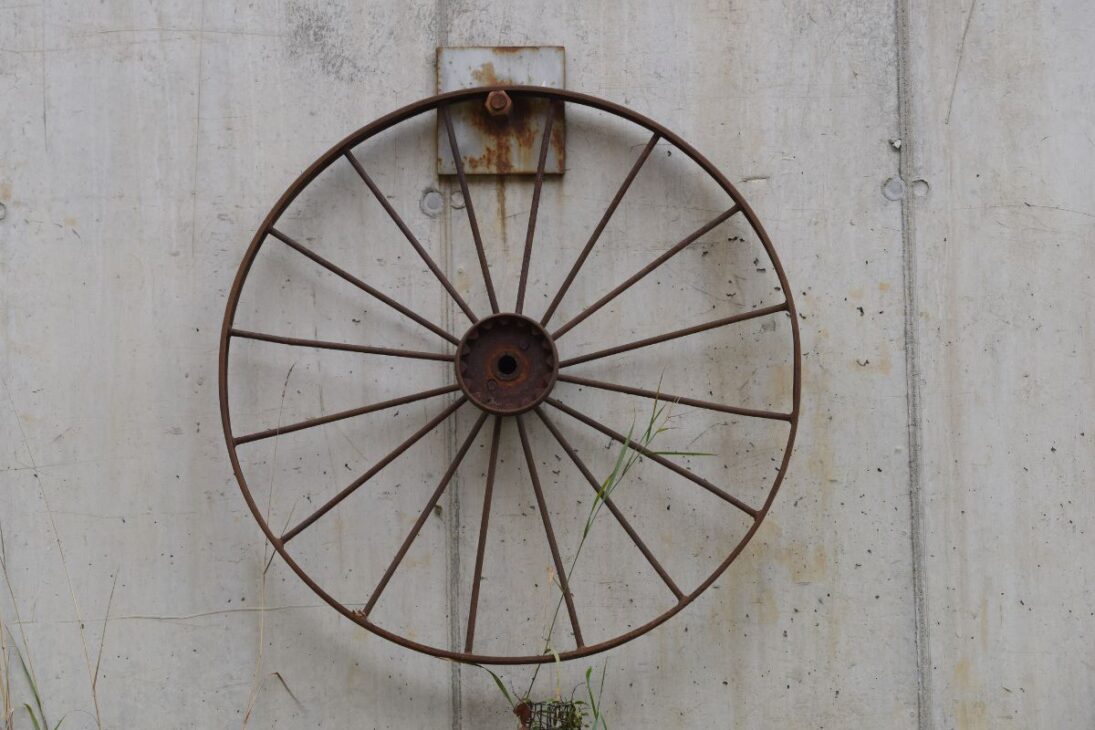 Roda antiga de ferro com sinais de ferrugem pendurada em uma parede de concreto, simbolizando o avanço industrial e a durabilidade das invenções.