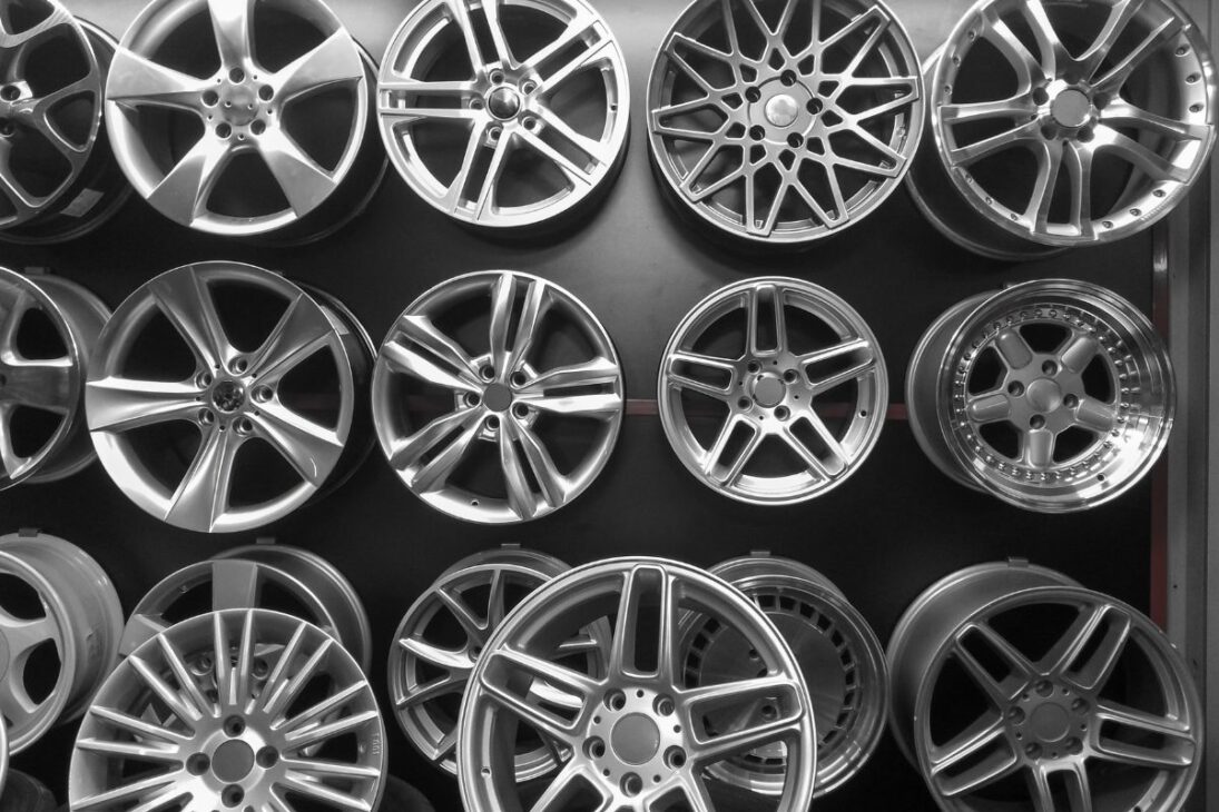 Várias rodas de liga leve com diferentes modelos e designs expostas em uma parede, destacando a variedade de estilos automotivos.

