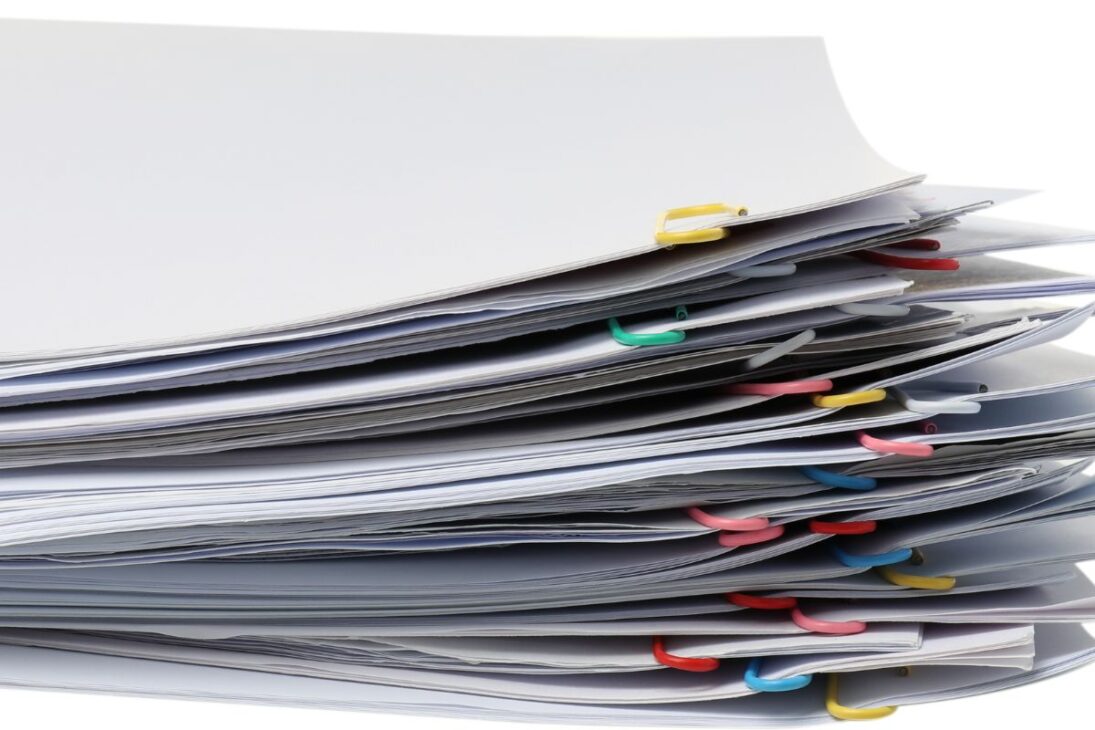 Uma pilha alta de papéis brancos, cada seção presa por clipes de papel de cores diferentes, contra um fundo branco.