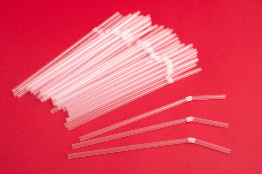 Pilha de canudos de plástico transparentes e alguns com articulação dobrável sobre um fundo vermelho vibrante.