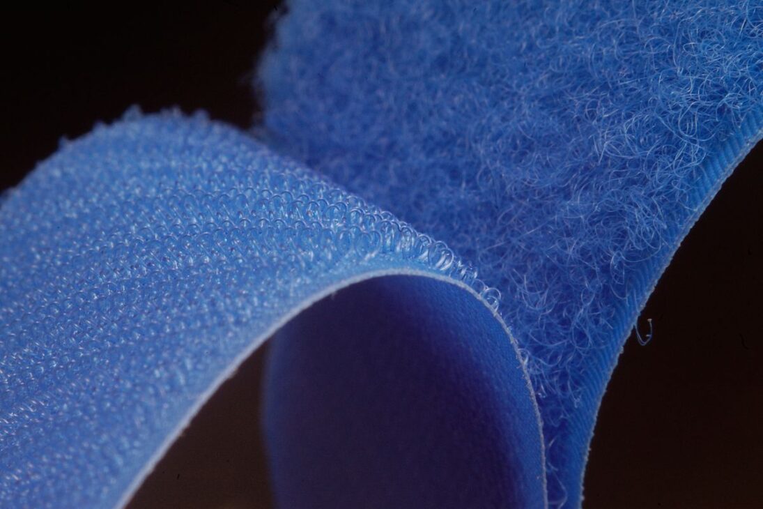 Vista ampliada de um fecho de velcro azul, mostrando a estrutura detalhada dos lados do gancho e do laço.