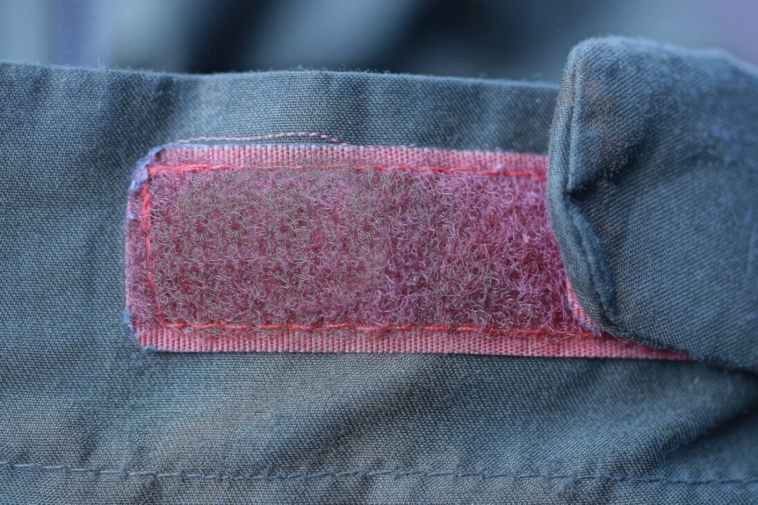 Close-up de um patch de velcro vermelho costurado em tecido verde, mostrando sinais de uso.