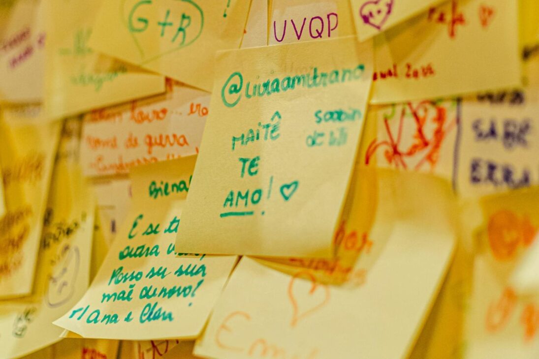 Parede coberta por uma coleção densa de post-its coloridos e amarelados com mensagens escritas à mão.