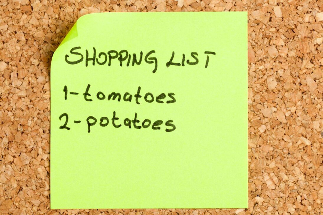  Post-it verde vibrante em um quadro de cortiça, exibindo uma lista de compras manuscrita.