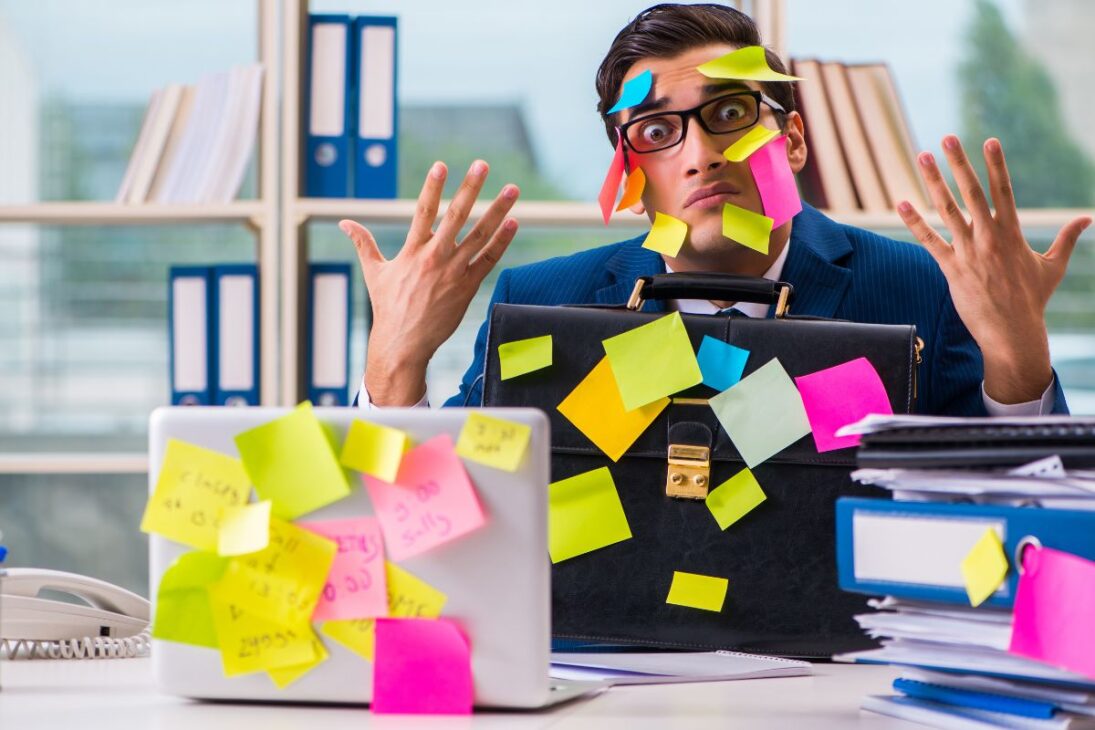 Homem de negócios sobrecarregado com post-its grudados no rosto e em objetos de escritório.