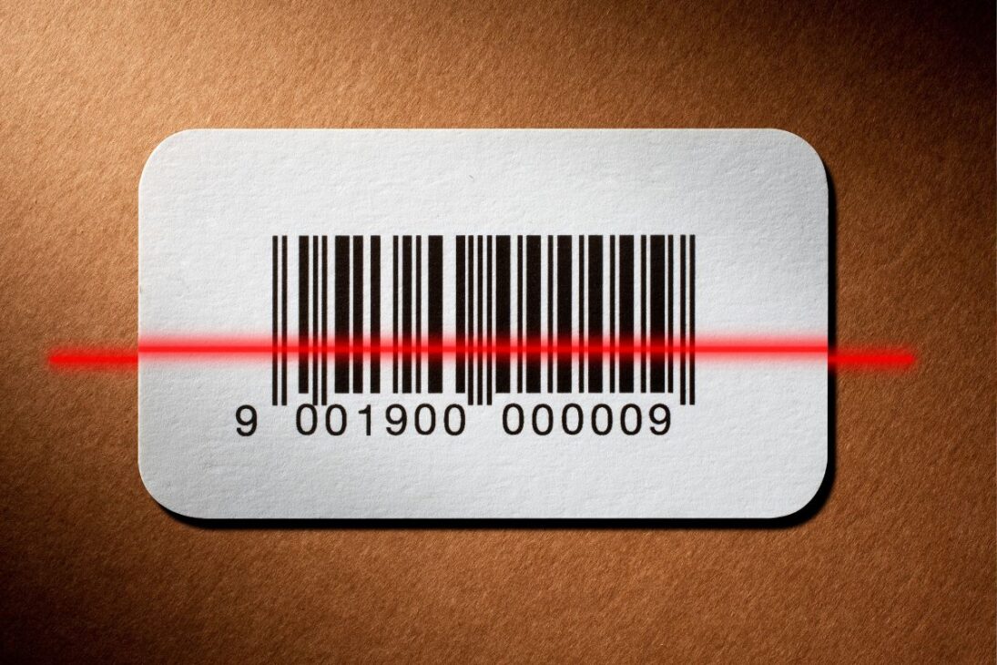 Código de barras branco sendo escaneado por um laser vermelho sobre fundo marrom texturizado.