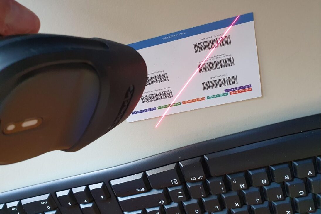 Scanner de código de barras portátil lendo etiquetas em um cartão, com teclado visível.