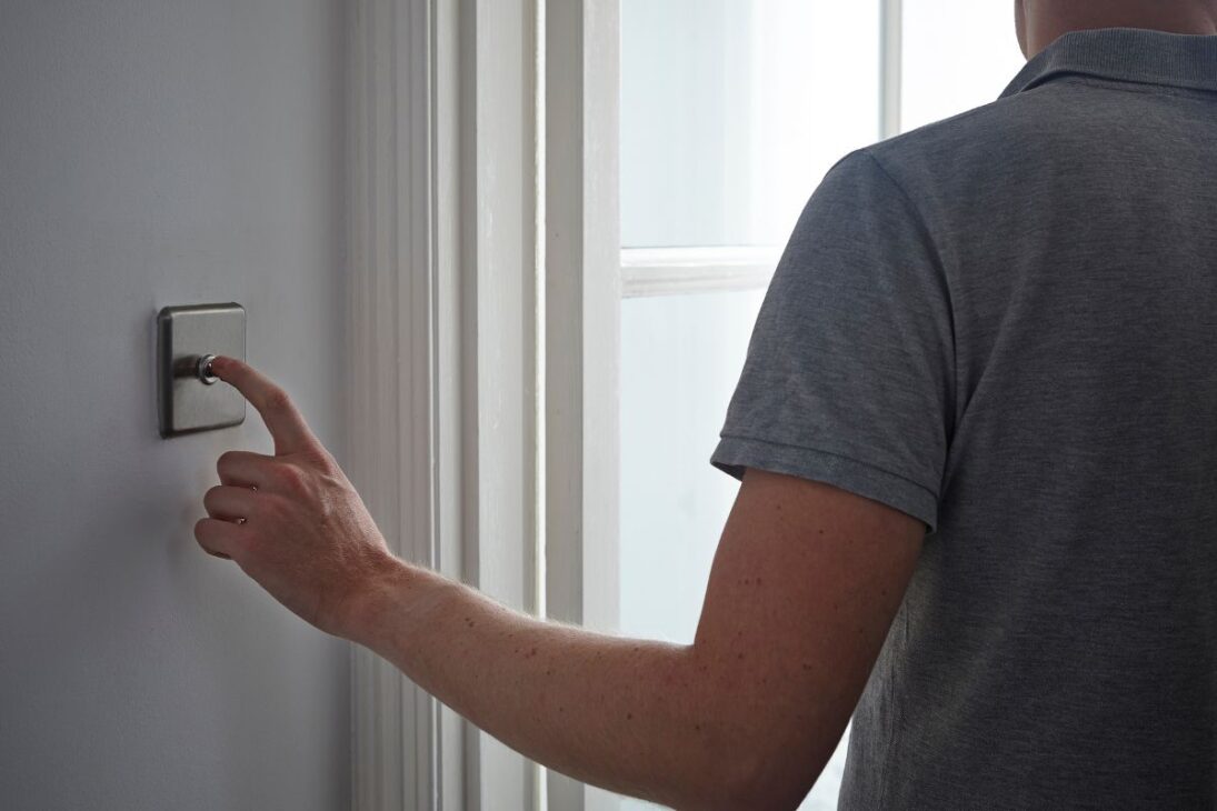 Homem de costas pressionando um interruptor de luz de metal escovado com um botão giratório.