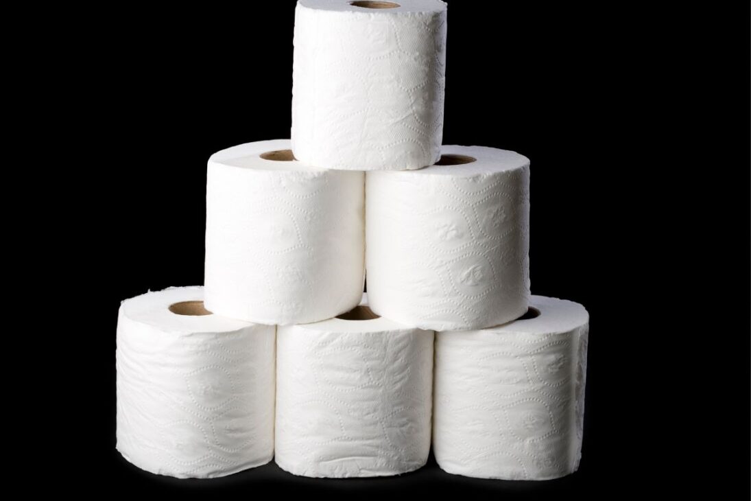 Pilha de rolos de papel higiênico branco sobre um fundo preto sólido.