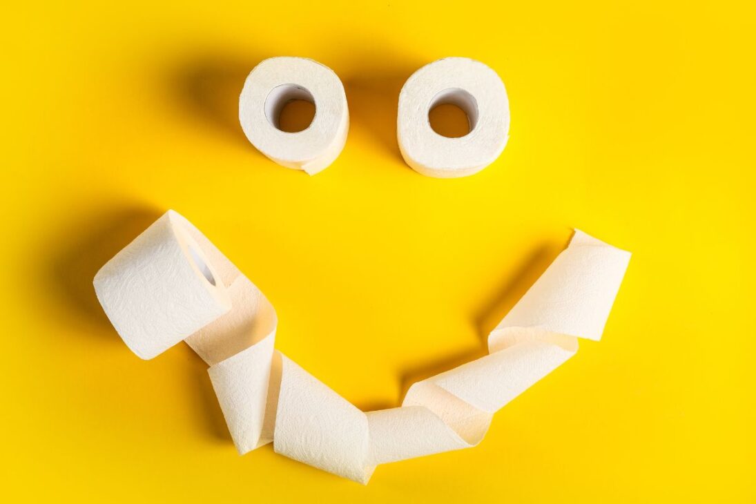 Rosto sorridente feito com rolos e papel higiênico desenrolado em um fundo amarelo.