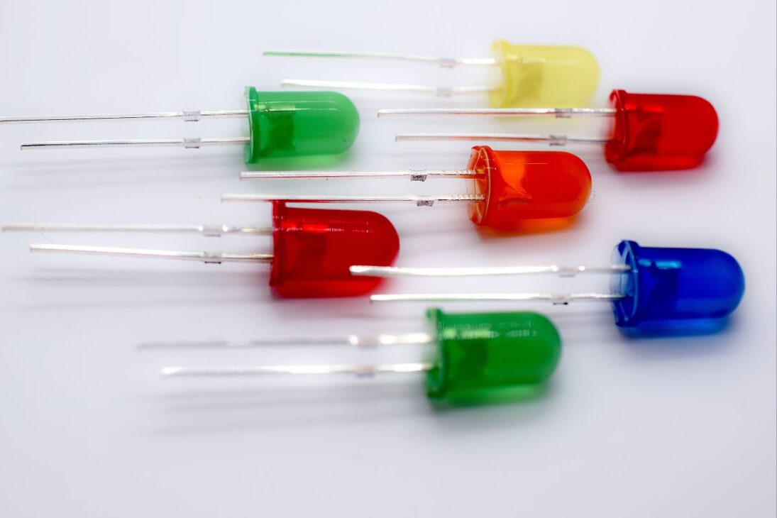  Uma fileira de diversos diodos emissores de luz (LEDs) coloridos, incluindo vermelho, verde, azul e amarelo, dispostos horizontalmente sobre uma superfície branca.