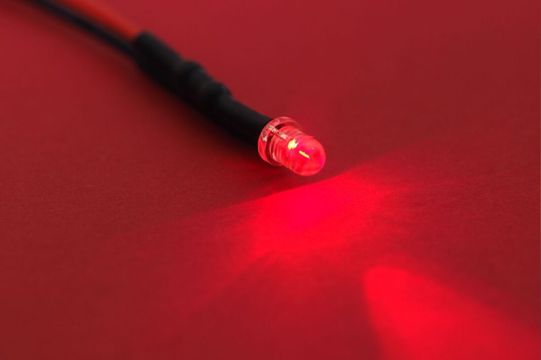 Um diodo emissor de luz (LED) vermelho aceso, emitindo um feixe de luz vibrante sobre uma superfície de papel vermelho, com um cabo preto conectado.