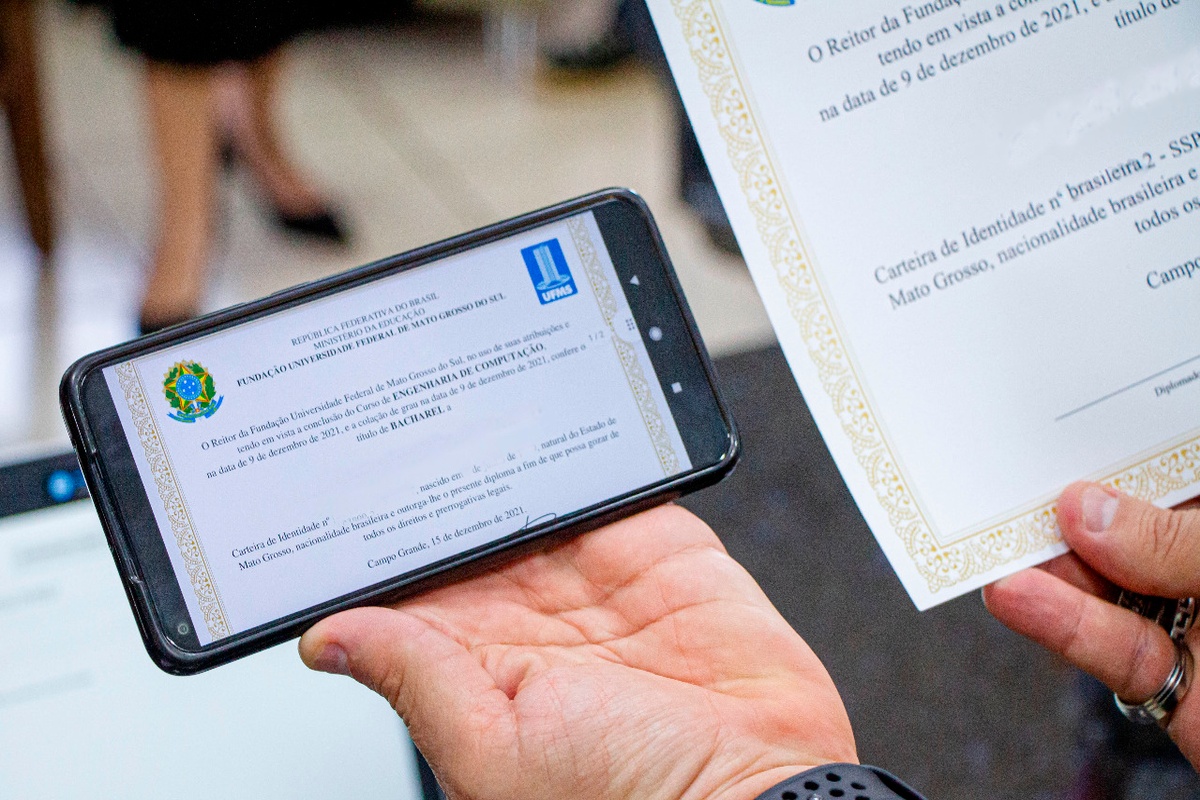 Pessoa exibindo diploma digital de graduação em smartphone e versão impressa