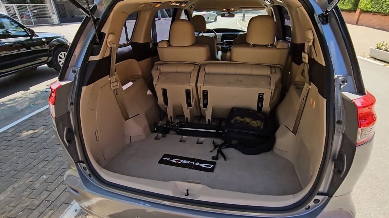 Porta-malas da Toyota Previa 2018 com a terceira fileira de bancos rebatida parcialmente, interior bege e bagagens visíveis no assoalho.