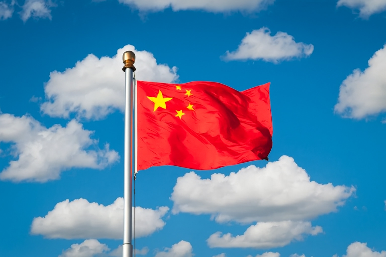 Bandeira da China hasteada em um mastro alto com céu azul e várias nuvens brancas ao fundo.