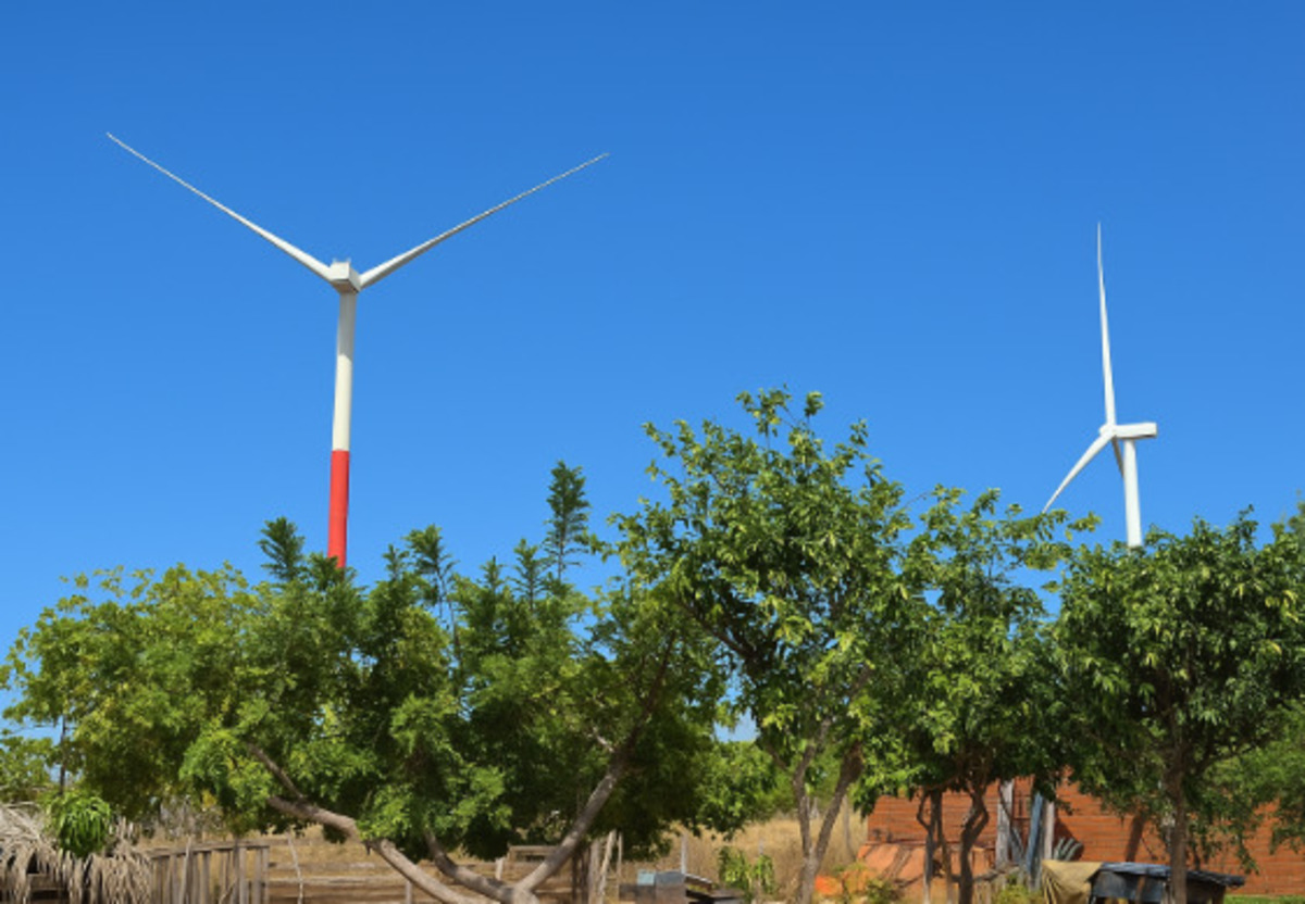 Aerogeradores de energia eólica em área rural com céu azul ao meio-dia.