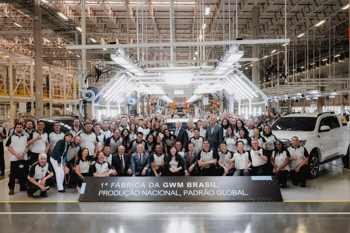 Funcionários posam na linha de montagem da GWM em fábrica brasileira com SUV branco ao fundo