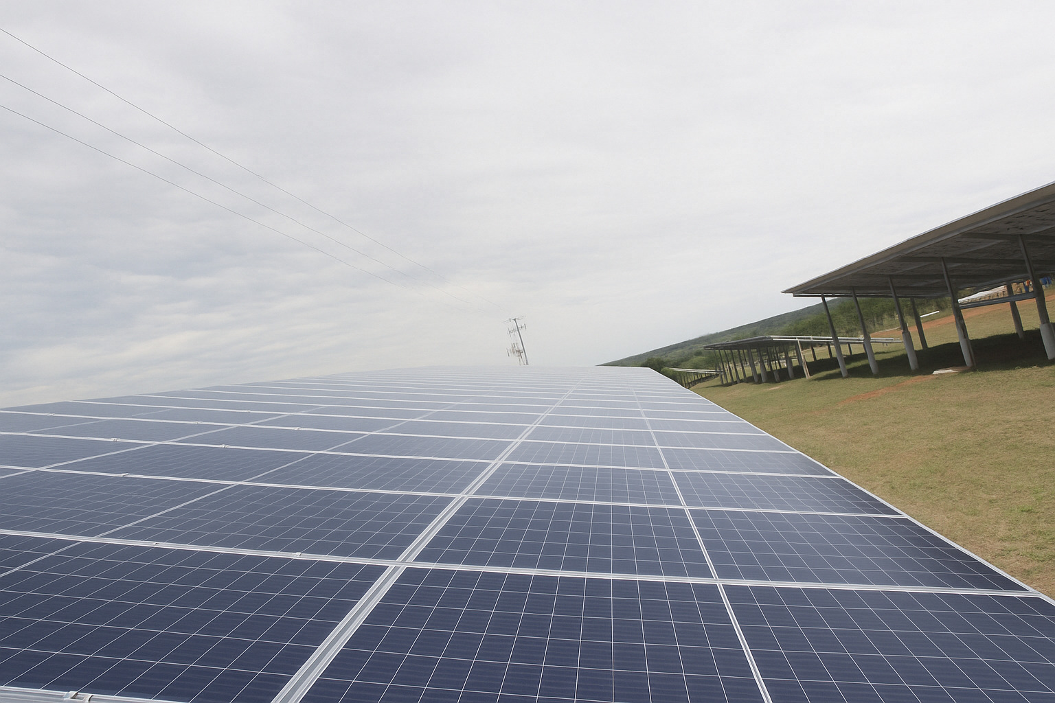 Painéis solares instalados em um campo aberto sob um céu de meio-dia levemente nublado.