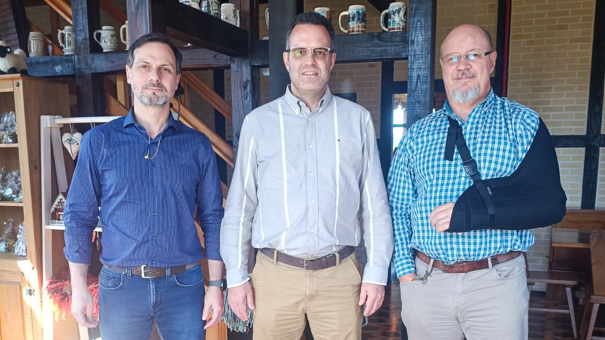 rês homens em ambiente corporativo, com destaque para o uso de tipoia no braço de um deles