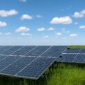 Painéis solares instalados em campo verde sob céu parcialmente nublado ao meio-dia.
