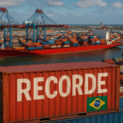 Porto brasileiro com navios cargueiros, contêineres e guindastes em operação destacando recorde histórico de 124,7 milhões de toneladas em julho de 2025.
