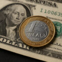 Moeda de um real sobre nota de dólar simbolizando a queda do dólar e valorização do real em 2025