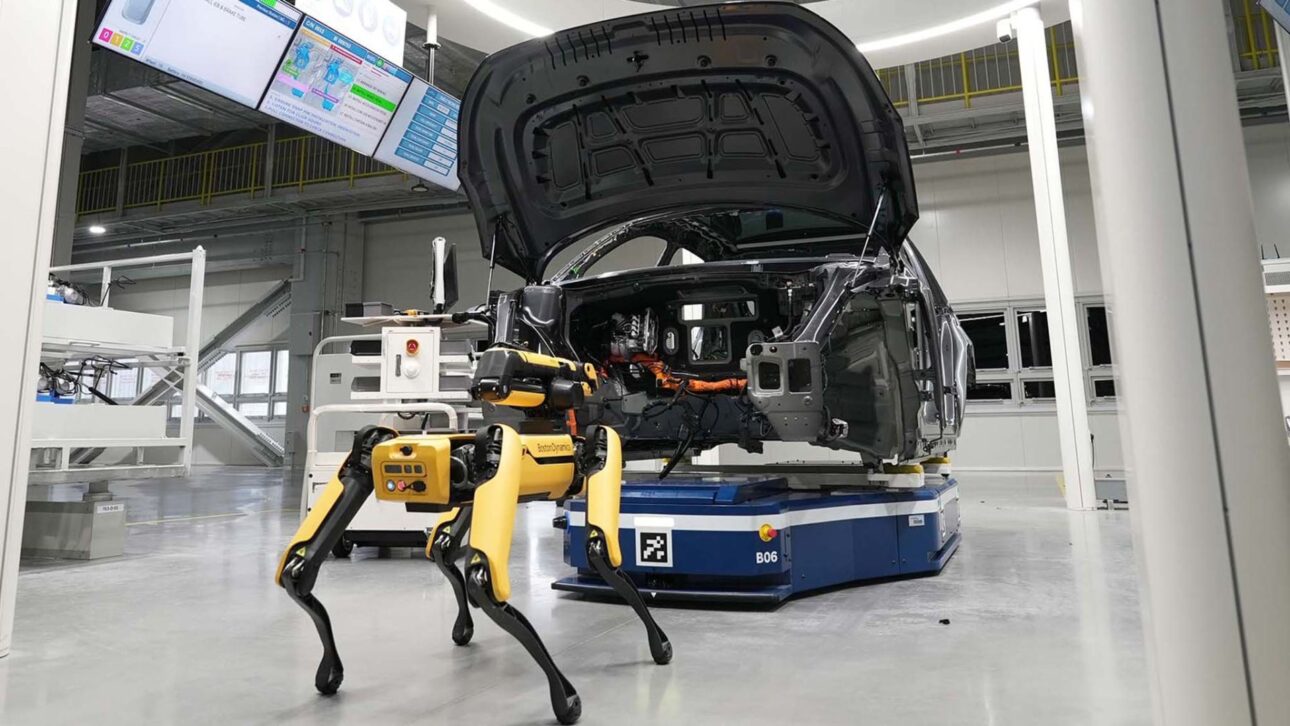 Spot farejando um veículo elétrico parcialmente montado, ilustrando a combinação de robôs avançados com inspeção automotiva de precisão.
(Imagem: MotorTrend — fábrica inteligente com cães-robôs em ação)
