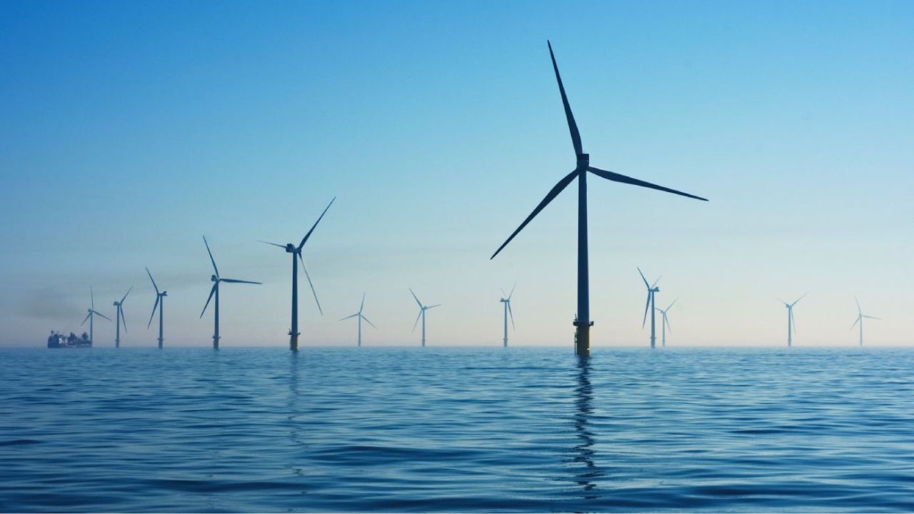 Parque eólico offshore com turbinas geradoras de energia renovável instaladas no oceano sob céu limpo, com embarcação ao fundo