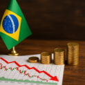 Gráfico de queda do PIB brasileiro com bandeira do Brasil e pilhas de moedas douradas.