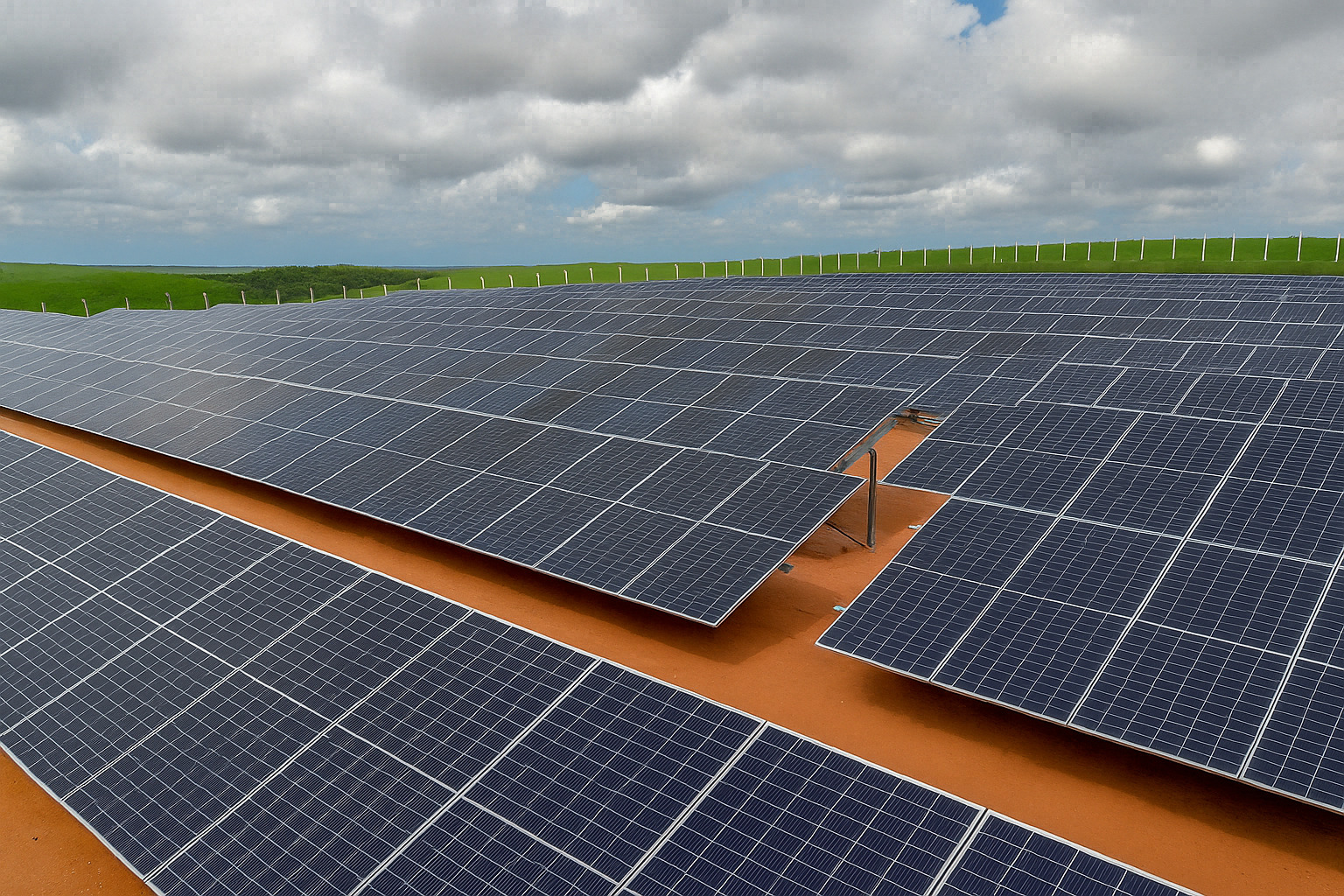 Usina solar com painéis fotovoltaicos sob céu nublado ao fundo.