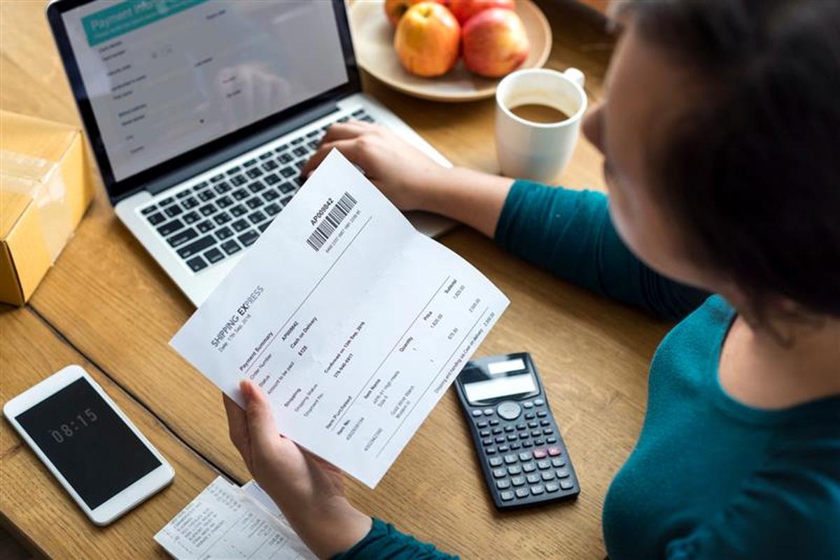 Pessoa analisa fatura eletrônica em frente ao computador com calculadora, simbolizando mudanças no faturamento com NF3e e NFCom.