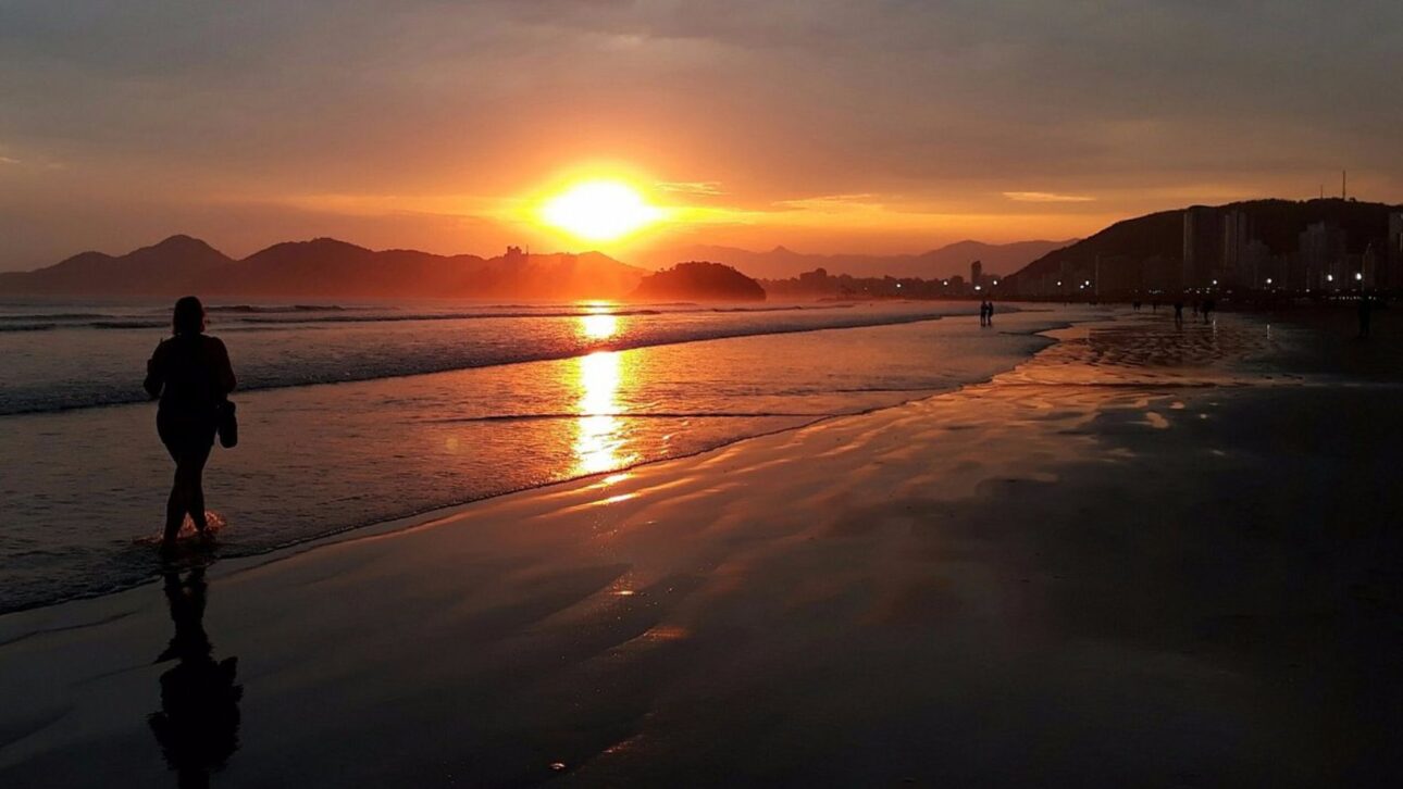 Pôr do sol refletido na faixa de areia, jardins e mar da orla de Santos-SP em momento tranquilo. (Imagem: Reprodução / Pinterest)