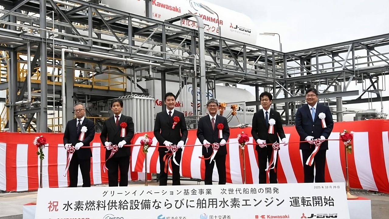 Executivos japoneses cortam fita em cerimônia de inauguração do primeiro motor marítimo a hidrogênio em terra, com instalações industriais ao fundo.