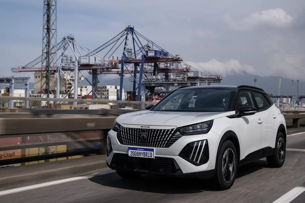 Peugeot 2008 Hybrid 2026 branco em movimento na estrada, com porto ao fundo, simbolizando eficiência, potência e tecnologia híbrida-leve.
