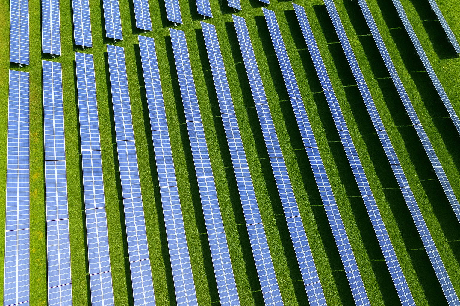Vista aérea de painéis solares alinhados sobre um campo verde, capturados em um dia ensolarado.