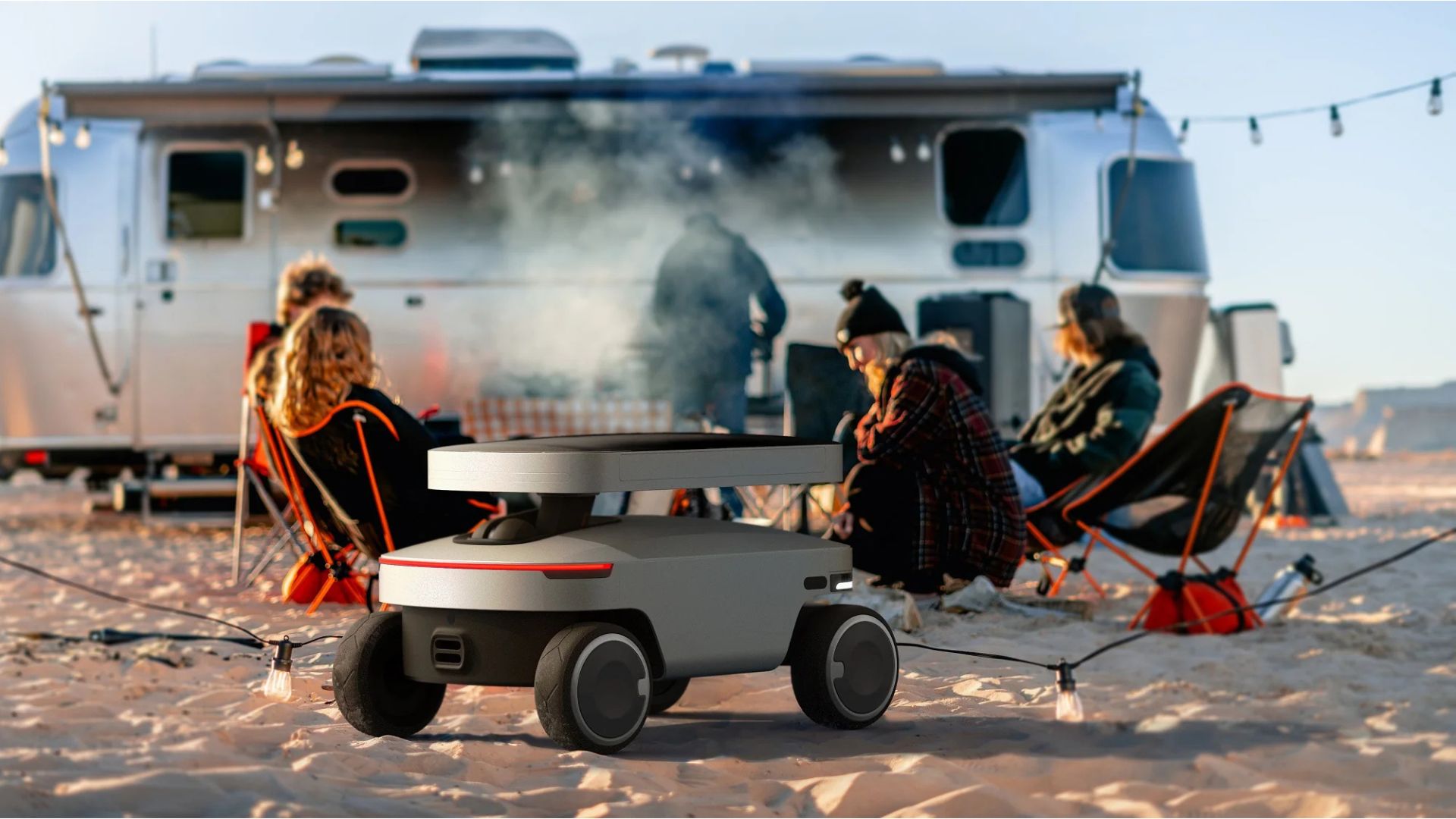 Robô Solar Mars Bot da Jackery atua como estação de energia portátil em ambiente externo durante acampamento, com pessoas ao fundo e trailer, ilustrando uso off-grid apresentado na CES 2026.