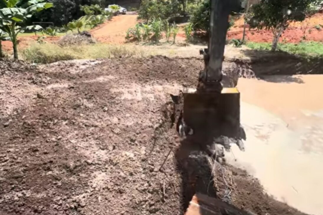 Operador com escavadeira adapta caixa seca, controla enxurrada e cria tanque de peixe em obra com lama e pouco espaço.