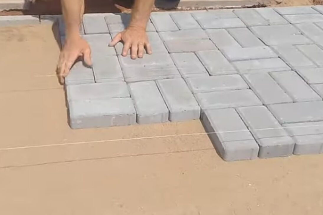 Pedreiro mostra bloquete intertravado na calçada com areia e placa vibratória para travar juntas e fechar acabamento.
