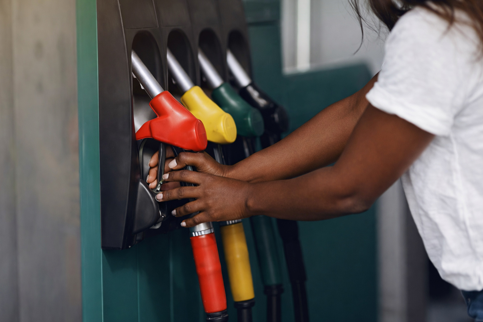 Mulher com pele negra segurando bomba de combustível em posto de gasolina.