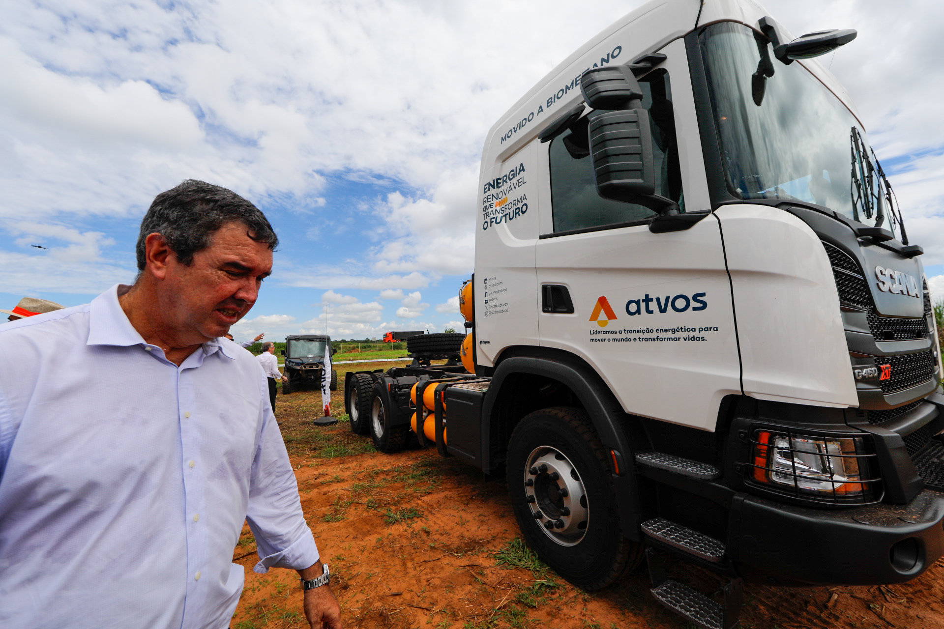 Homem ao lado de caminhão movido a biometano em área rural com céu parcialmente nublado.