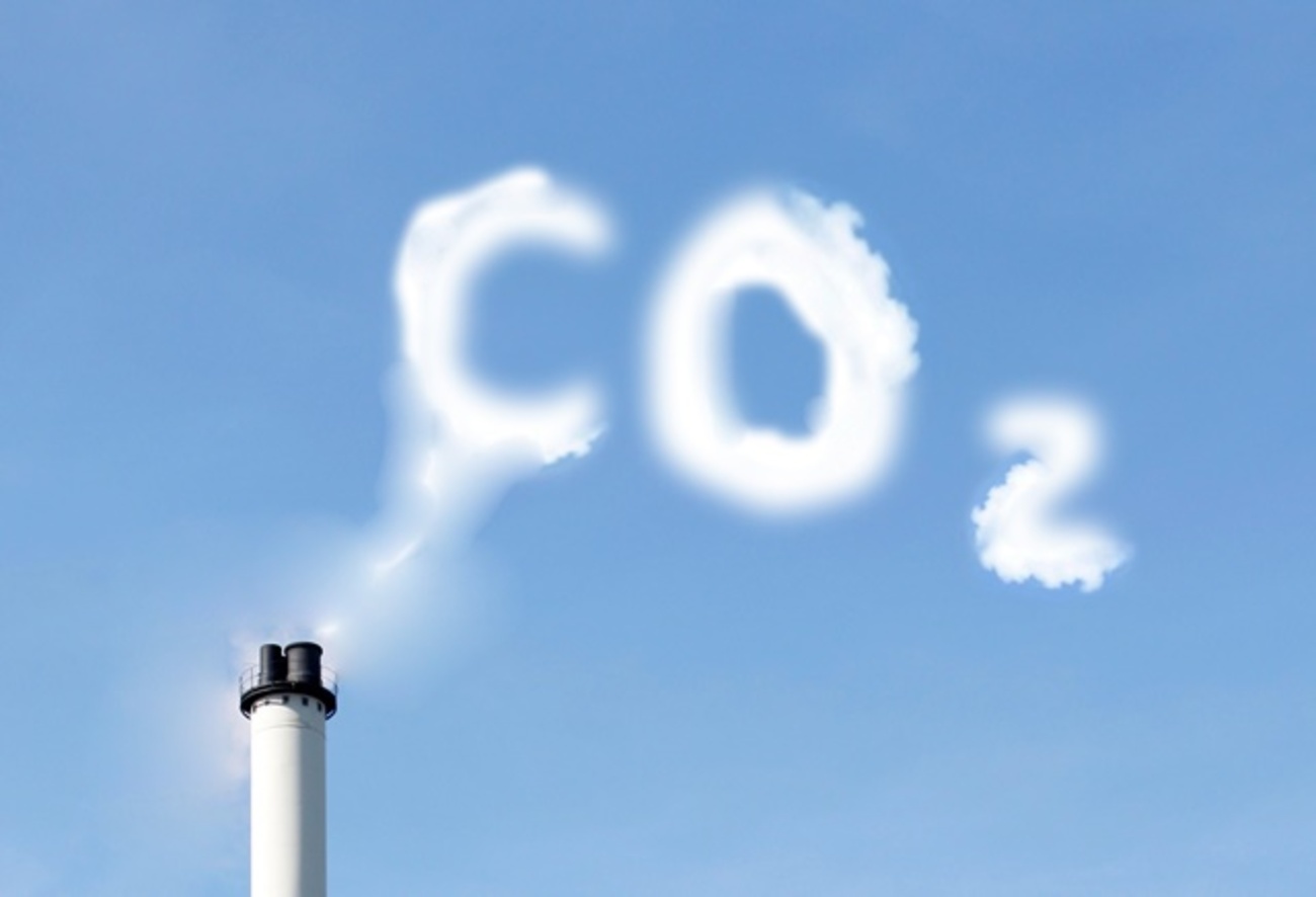 Chaminé industrial emitindo fumaça que forma a palavra CO2 no céu azul.