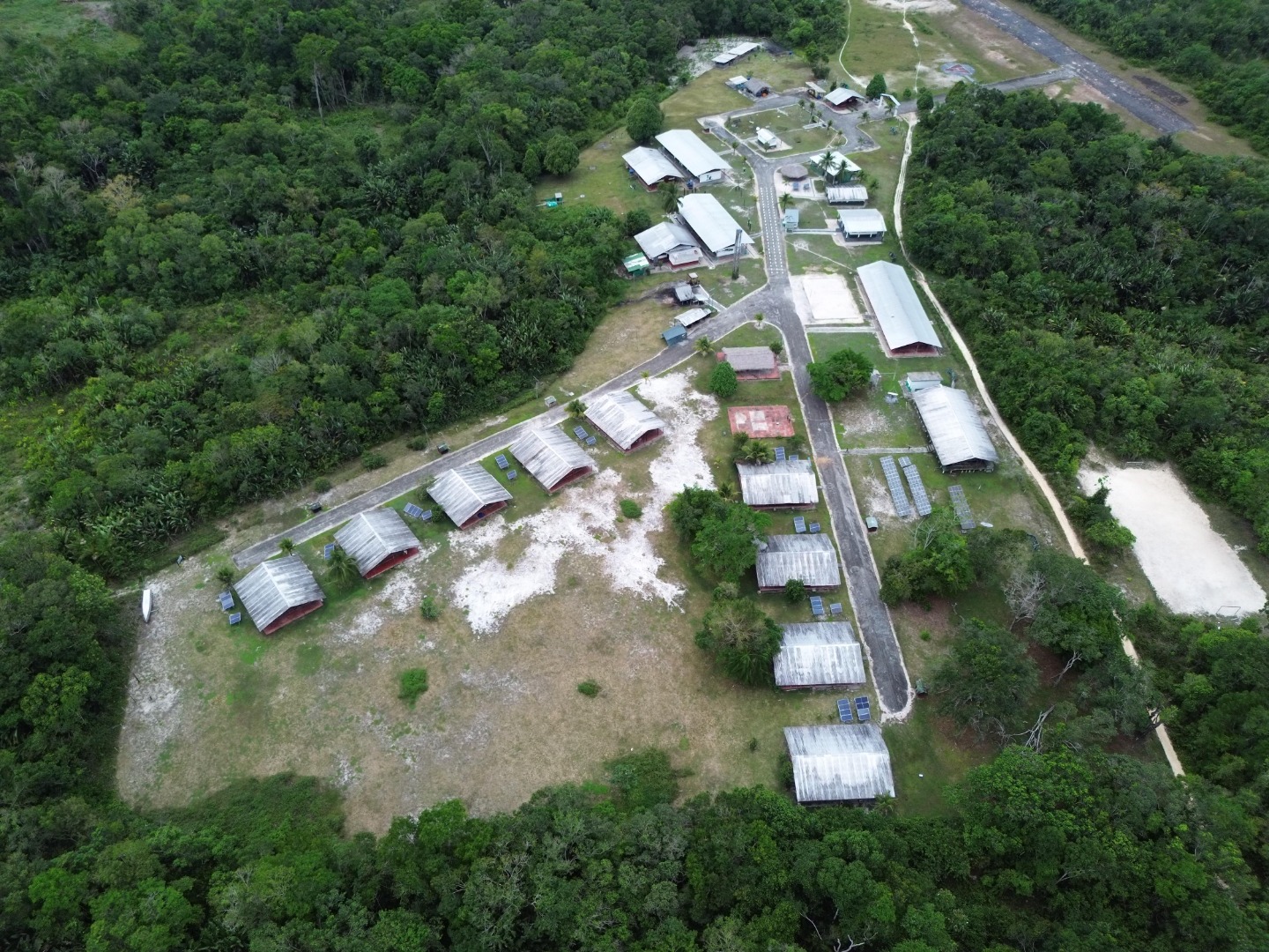 Vista aérea de comunidade rural cercada por floresta com casas e pequenos sistemas de energia solar
