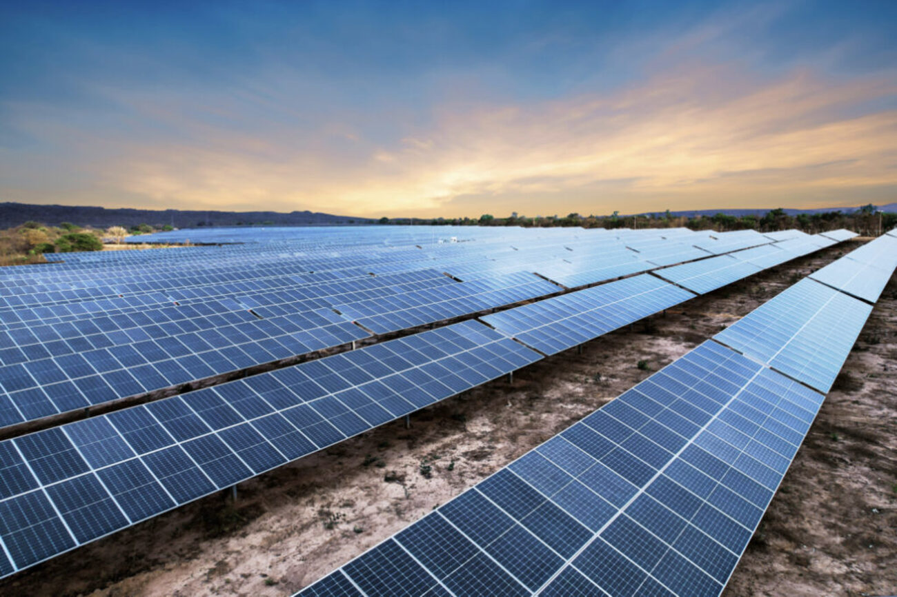 Grande usina de energia solar com fileiras de painéis fotovoltaicos ao pôr do sol em área aberta.