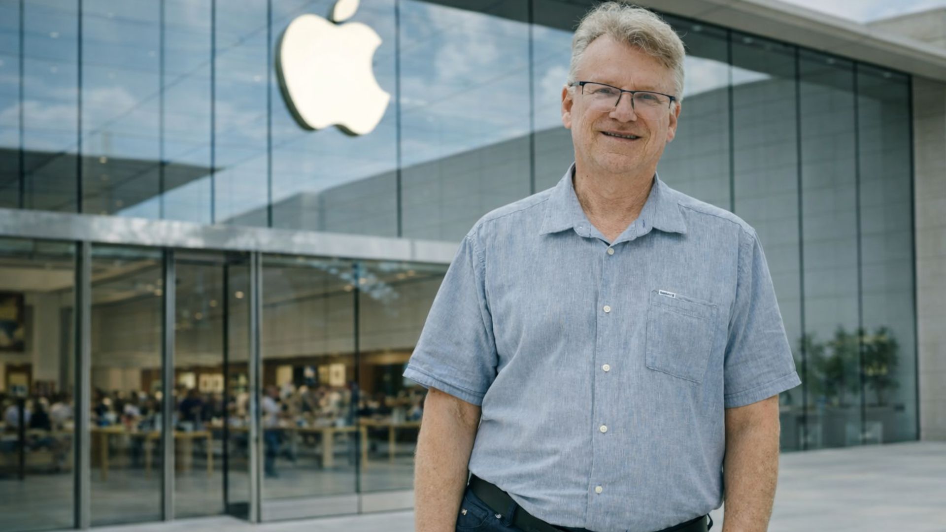 Chris Espinosa, funcionário mais antigo da Apple, em frente a uma loja da empresa com logotipo ao fundo, destacando sua trajetória na big tech