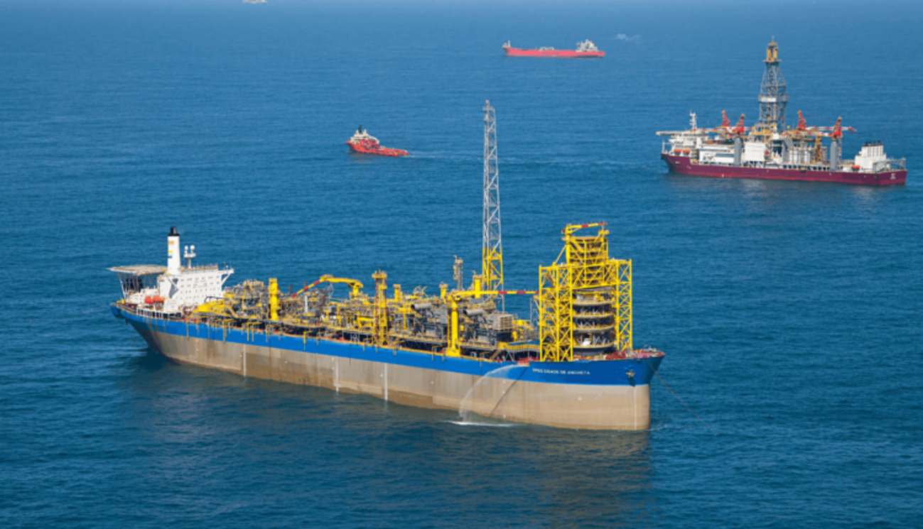 Navio-plataforma de petróleo em alto-mar com embarcações de apoio e plataforma de perfuração ao fundo.